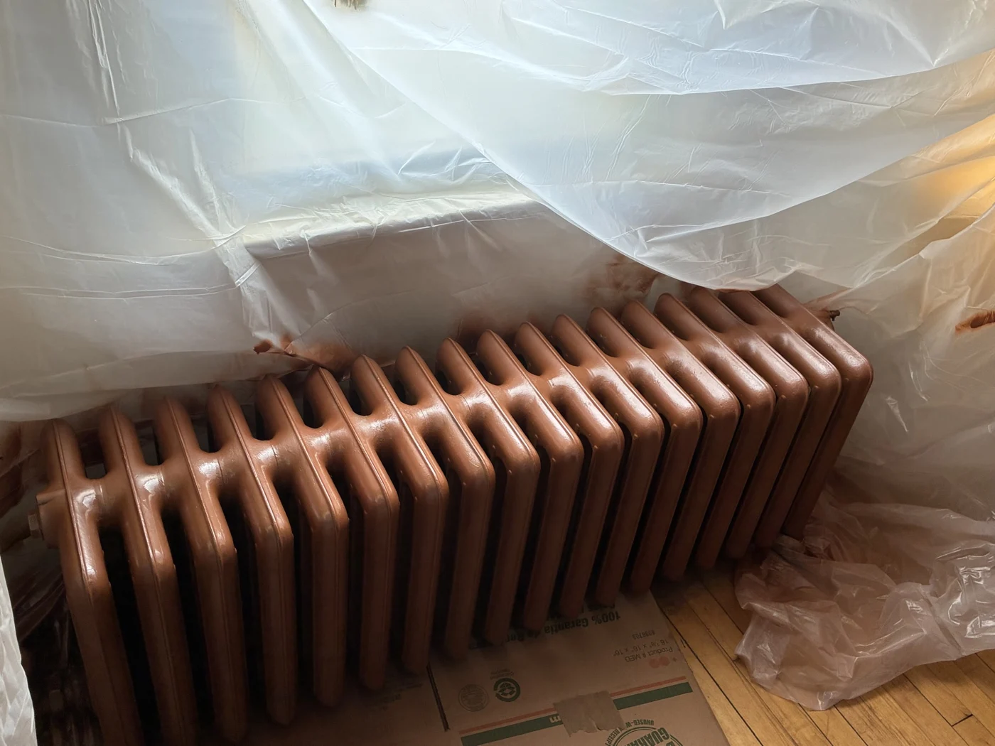 Copper-toned radiator surrounded by protective plastic and cardboard.