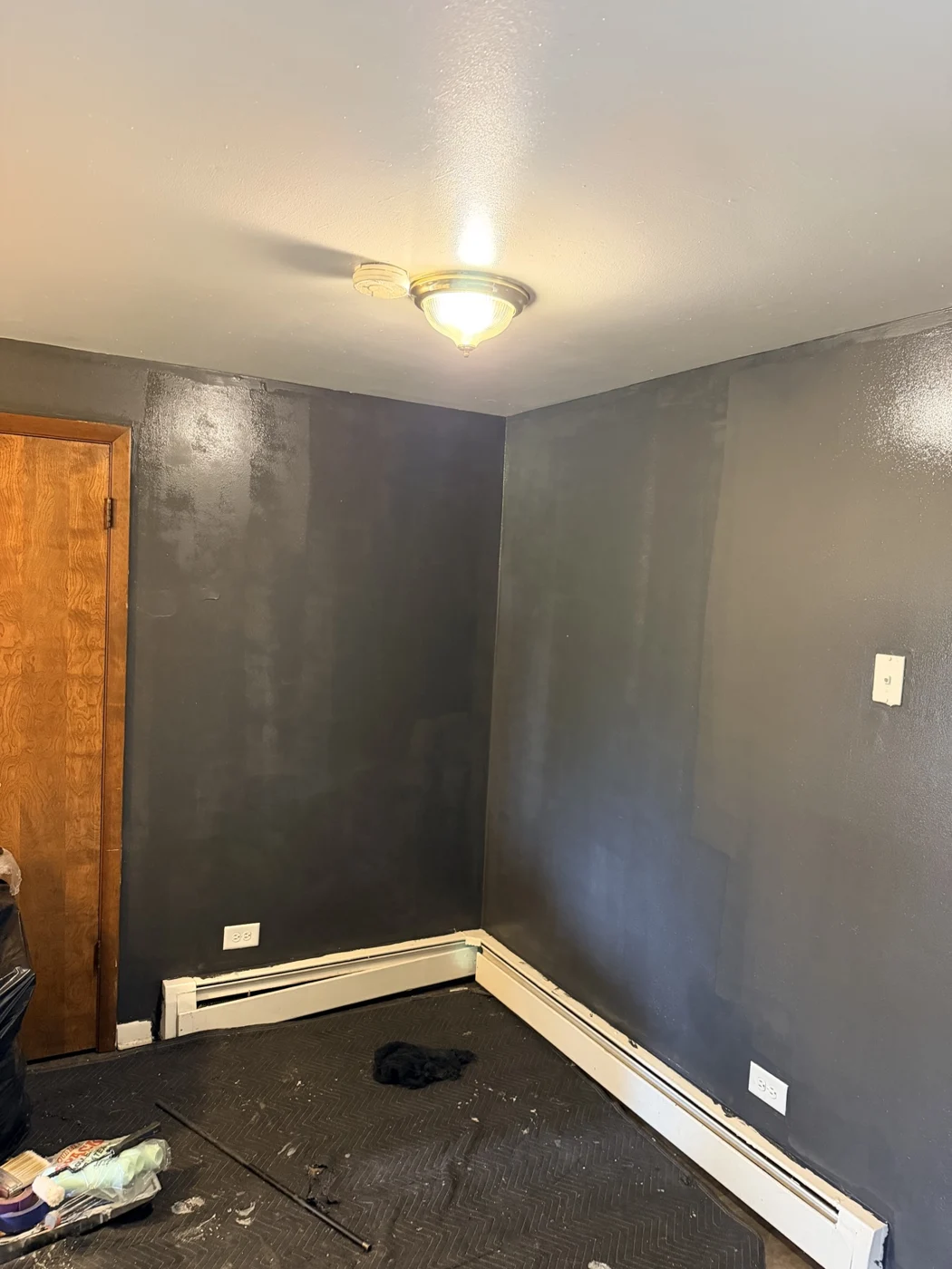 Interior room with gray walls, a white ceiling, and protective floor covering during painting.