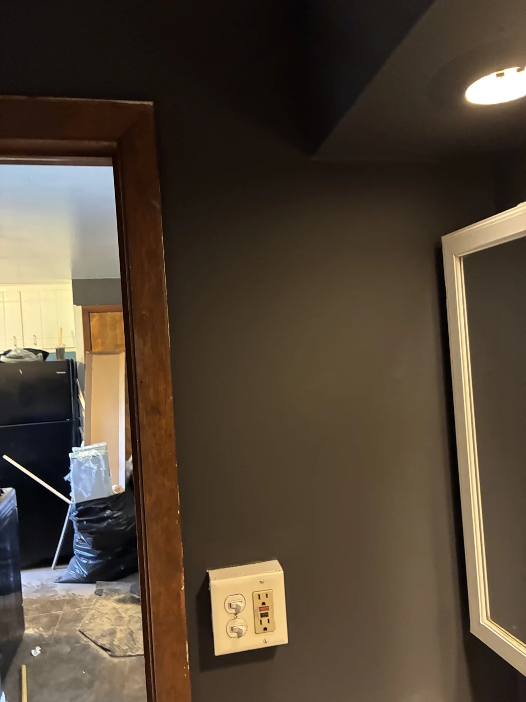 Dark wall beside a wood-trimmed doorway and a light-framed mirror.